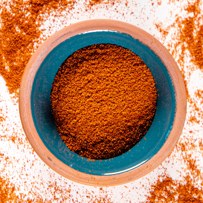 Cayenne Pepper powder herb in blue clay bowl with white background and herb surrounding.
