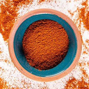 Cayenne Pepper powder herb in blue clay bowl with white background and herb surrounding.