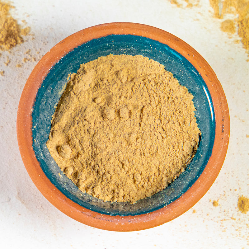 Maca powder herb in blue clay bowl with white background and herb surrounding.