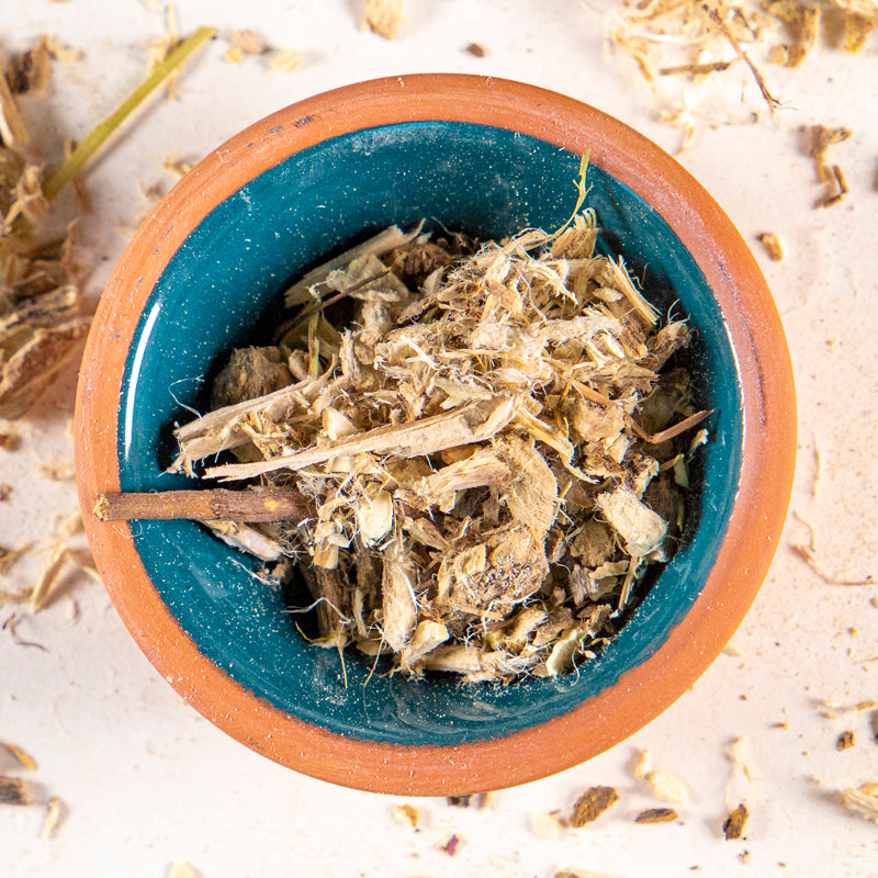 Marshmallow root herb in blue clay bowl with white background and herb surrounding.