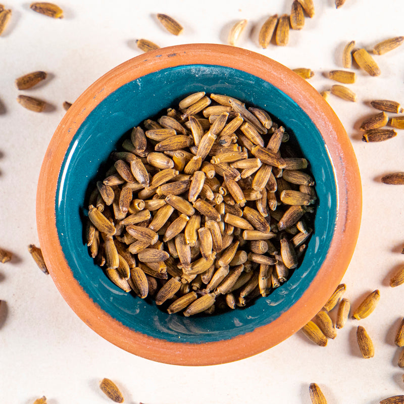 Milk Thistle Seed Whole herb in blue clay bowl with white background and herb surrounding.