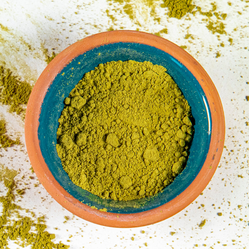 Moringa Powder herb in blue clay bowl with white background and herb surrounding.