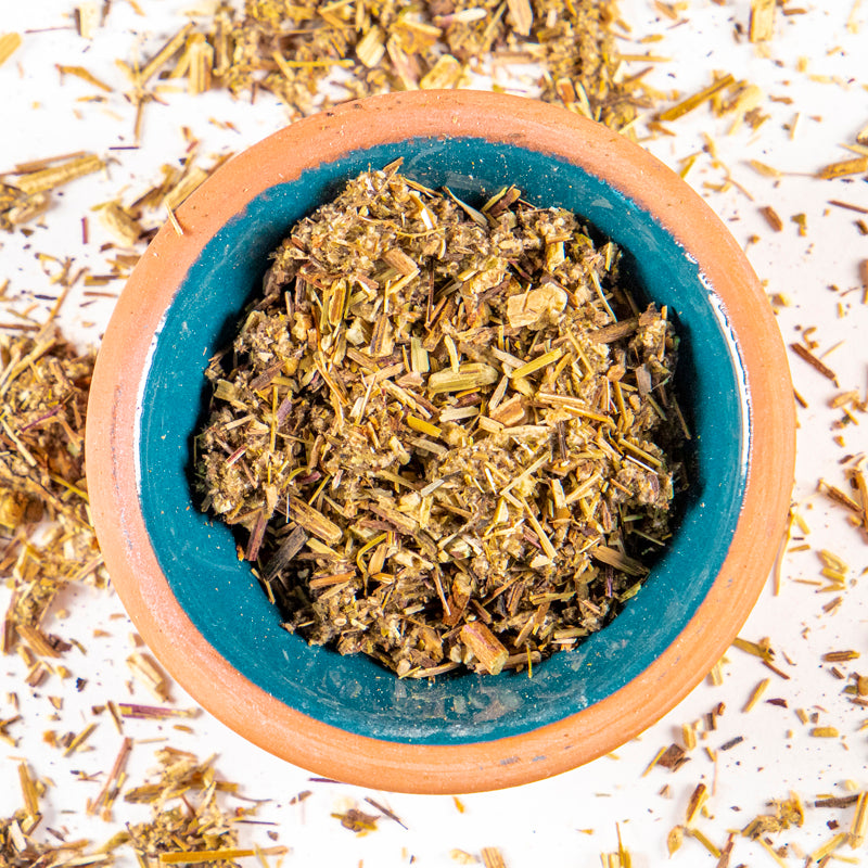 Mugwort herb in blue clay bowl with white background and herb surrounding.