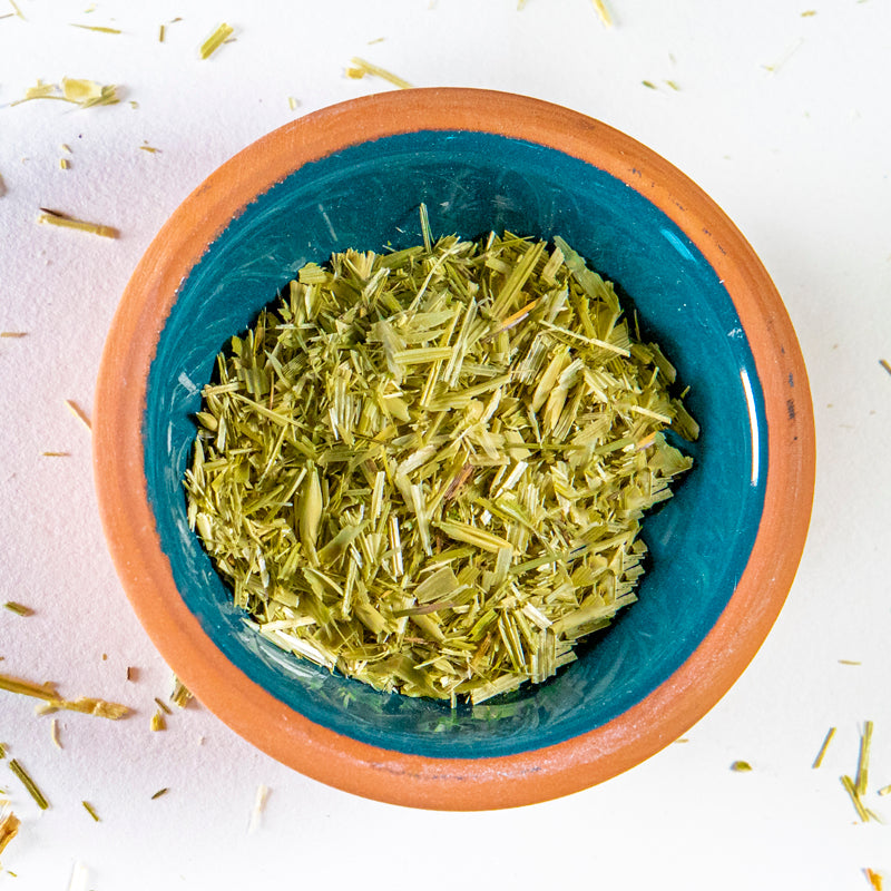 Oatstraw herb in blue clay bowl with white background and herb surrounding.