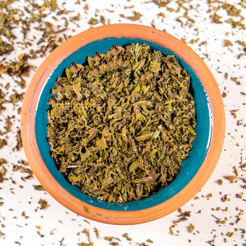 Peppermint Leaves herb in blue clay bowl with white background and herb surrounding.