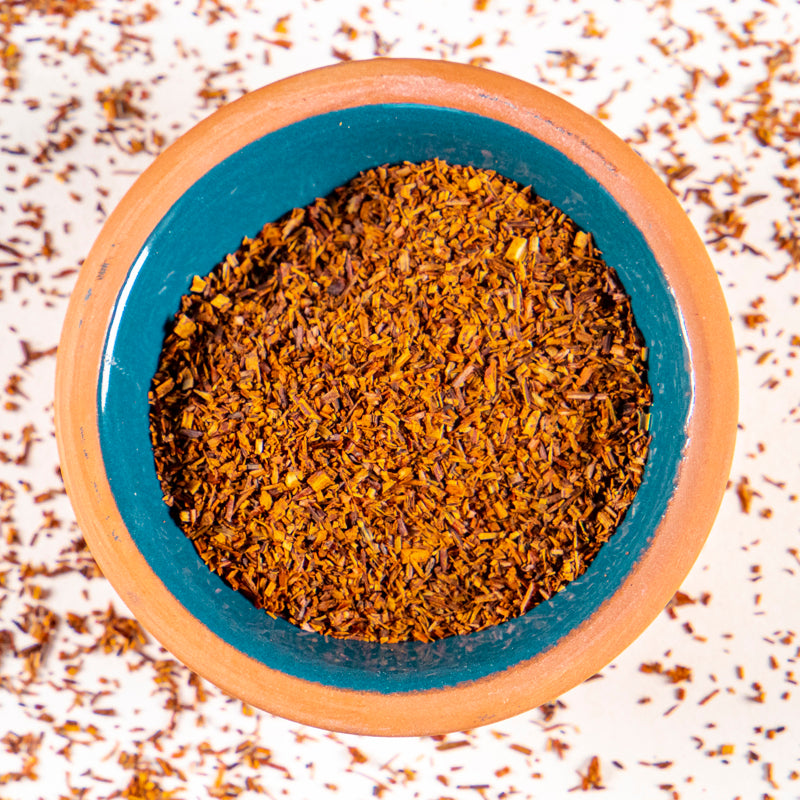 Rooibos herb in blue clay bowl with white background and herb surrounding.