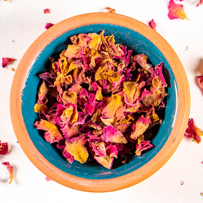 Rose Buds and Petals herb in blue clay bowl with white background and herb surrounding.