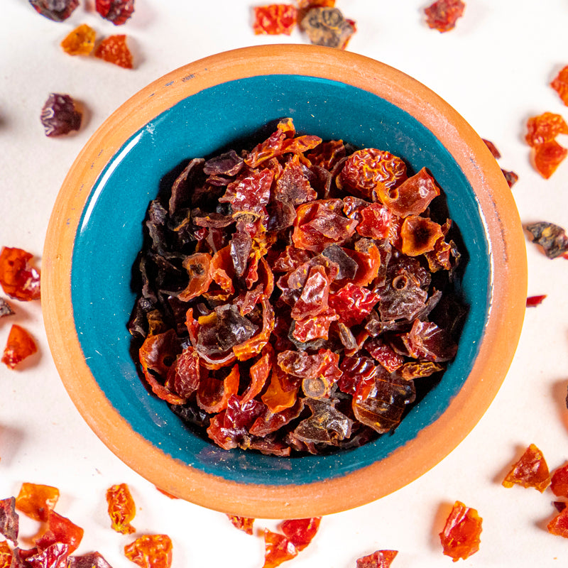 Rosehips herb in blue clay bowl with white background and herb surrounding.