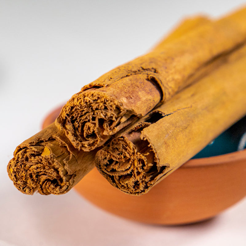Ceylon Cinnamon in blue clay bowl with white background and herb surrounding.